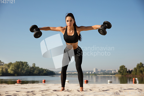 Image of Young healthy female athlete doing workout at the beach