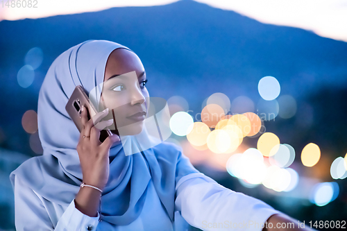 Image of Young Muslim woman on  street at night using phone