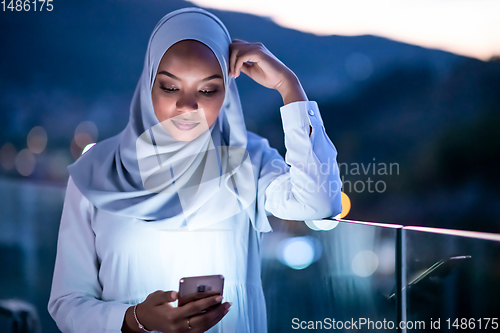 Image of Young Muslim woman on  street at night using phone