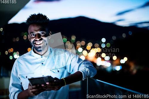 Image of Young  Afro man on street at night using tablet computer