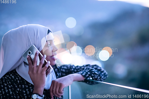 Image of Young Muslim woman on  street at night using phone