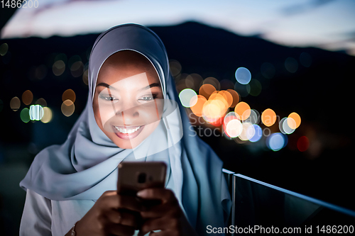 Image of Young Muslim woman on  street at night using phone