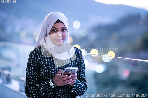 Image of Young Muslim woman on  street at night using phone