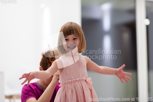 Image of young mother helping daughter while putting on a dress