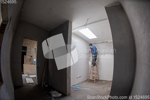 Image of construction worker using ladder while plastering on gypsum wall