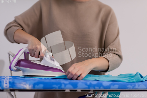 Image of Red haired woman ironing clothes at home
