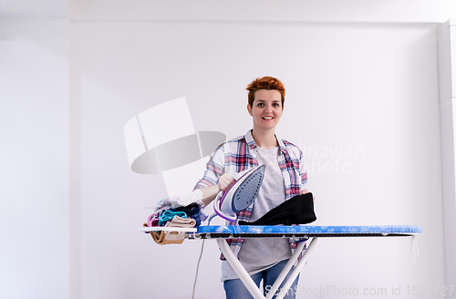 Image of Red haired woman ironing clothes at home