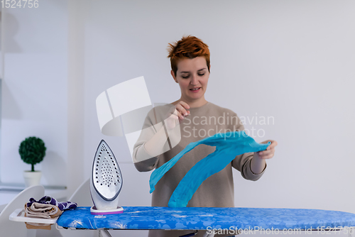 Image of Red haired woman ironing clothes at home