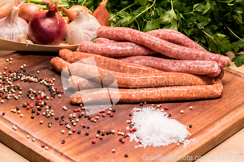 Image of raw sausages with chilli and herbs on a wooden board with spices