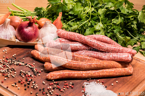 Image of raw sausages with chilli and herbs on a wooden board with spices