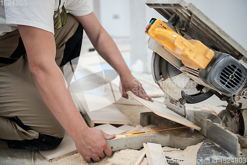 Image of Man cutting laminate floor plank with electrical circular saw