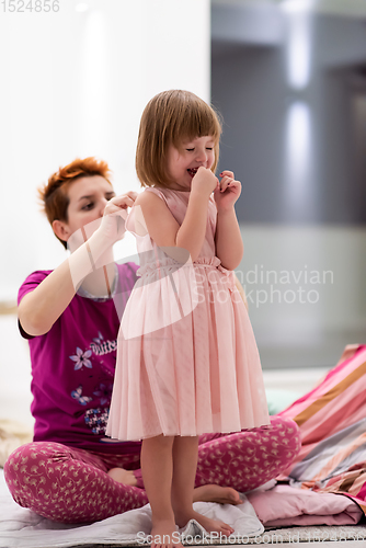 Image of young mother helping daughter while putting on a dress
