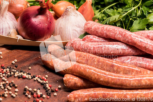 Image of raw sausages with chilli and herbs on a wooden board with spices