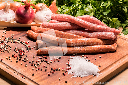 Image of raw sausages with chilli and herbs on a wooden board with spices