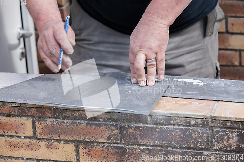 Image of the tiler measures and puts marks to cut and lay a tile