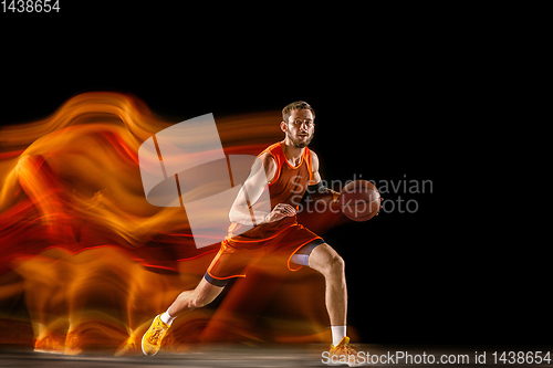 Image of Young caucasian basketball player against dark background in mixed light