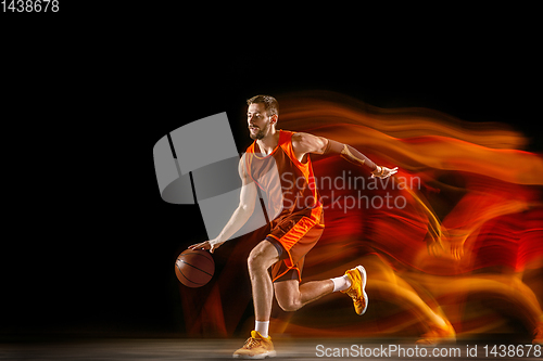 Image of Young caucasian basketball player against dark background in mixed light