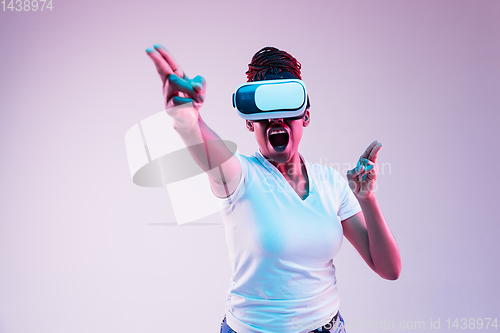 Image of Young african-american woman\'s using VR-glasses in neon light