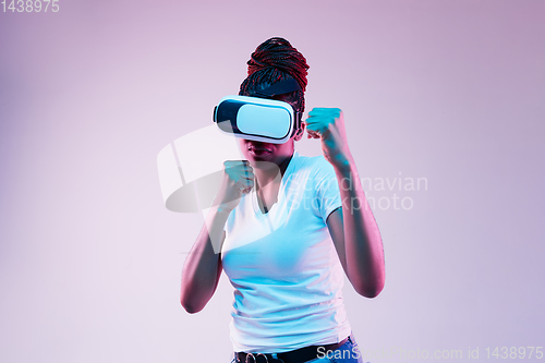 Image of Young african-american woman\'s using VR-glasses in neon light