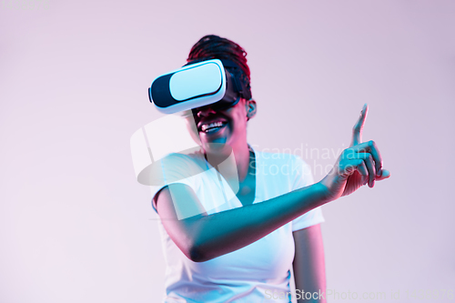 Image of Young african-american woman\'s using VR-glasses in neon light