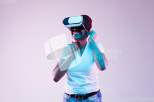 Image of Young african-american woman\'s using VR-glasses in neon light