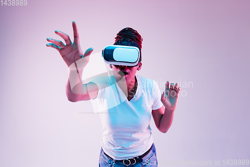 Image of Young african-american woman\'s using VR-glasses in neon light