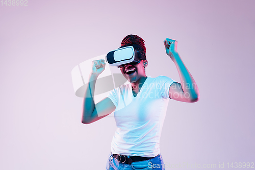 Image of Young african-american woman\'s using VR-glasses in neon light