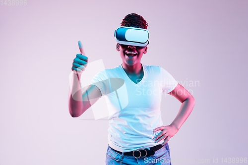 Image of Young african-american woman\'s using VR-glasses in neon light