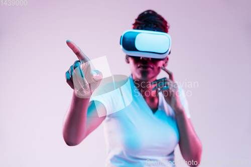 Image of Young african-american woman\'s using VR-glasses in neon light