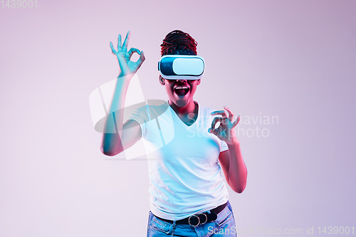 Image of Young african-american woman\'s using VR-glasses in neon light