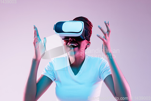 Image of Young african-american woman\'s using VR-glasses in neon light