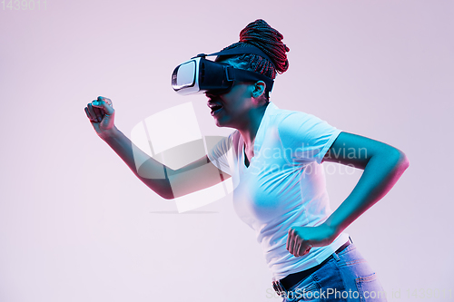 Image of Young african-american woman\'s using VR-glasses in neon light