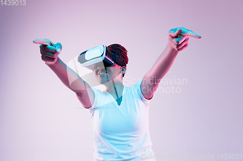 Image of Young african-american woman\'s using VR-glasses in neon light