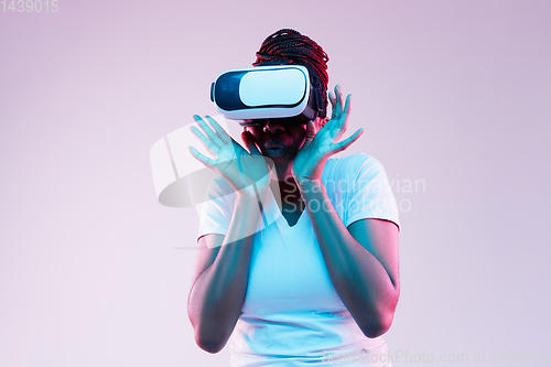Image of Young african-american woman\'s using VR-glasses in neon light
