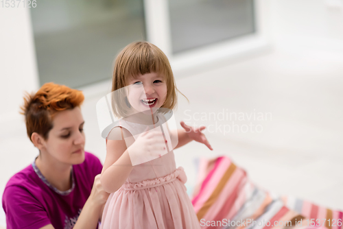 Image of young mother helping daughter while putting on a dress