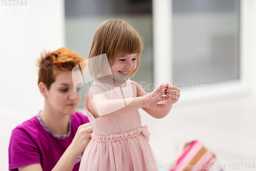 Image of young mother helping daughter while putting on a dress