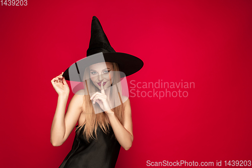 Image of Young woman in hat as a witch on red background