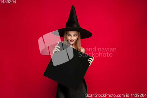 Image of Young woman in hat as a witch on red background