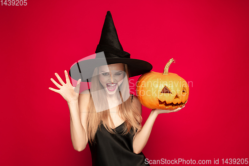 Image of Young woman in hat as a witch on red background