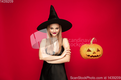 Image of Young woman in hat as a witch on red background