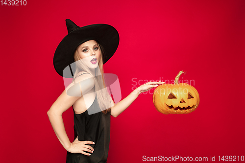 Image of Young woman in hat as a witch on red background