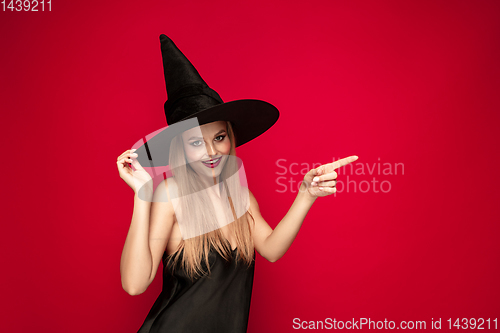 Image of Young woman in hat as a witch on red background