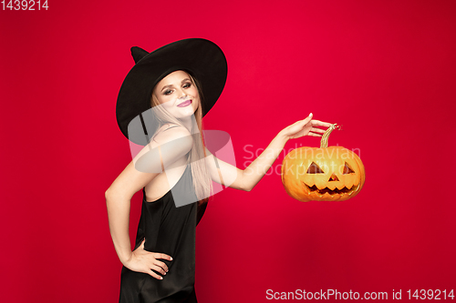 Image of Young woman in hat as a witch on red background
