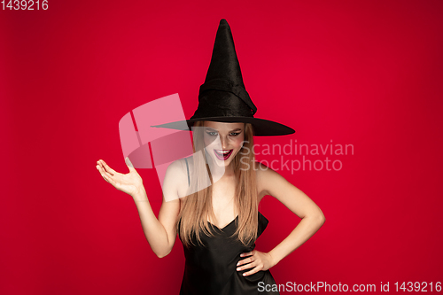 Image of Young woman in hat as a witch on red background