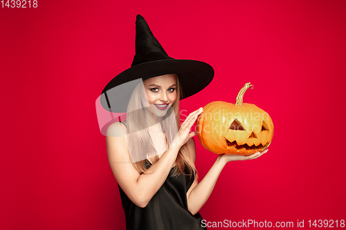 Image of Young woman in hat as a witch on red background