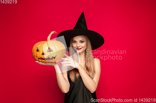Image of Young woman in hat as a witch on red background