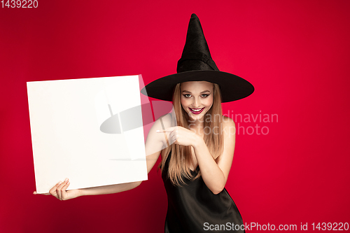 Image of Young woman in hat as a witch on red background