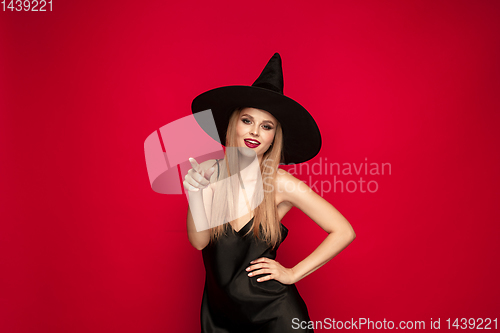 Image of Young woman in hat as a witch on red background