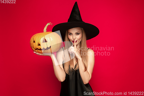 Image of Young woman in hat as a witch on red background