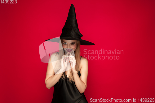 Image of Young woman in hat as a witch on red background